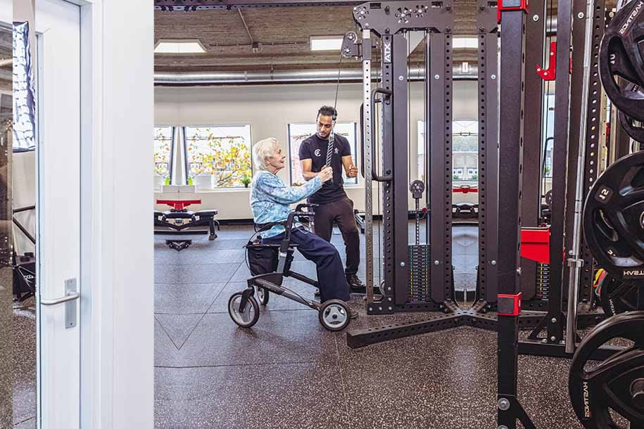 Personal trainer begeleidt senior op trainingsapparaat in moderne fitnessruimte