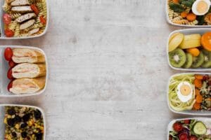 Maaltijdboxen met pasta, vlees, brood, groenten, fruit en salade in plastic bakjes op wit aanrecht