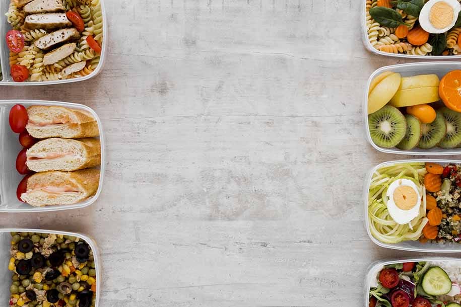 Maaltijdboxen met pasta, vlees, brood, groenten, fruit en salade in plastic bakjes op wit aanrecht