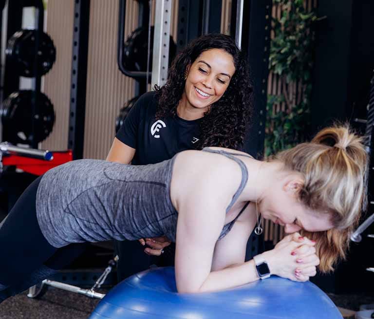 Personal trainer begeleidt vrouw bij stabiliteitsbal oefening in fitnessruimte