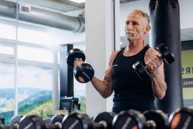 Man voert bicepsoefeningmet dumbbells uit in een moderne trainingsruimte met uitzicht op een berglandschap