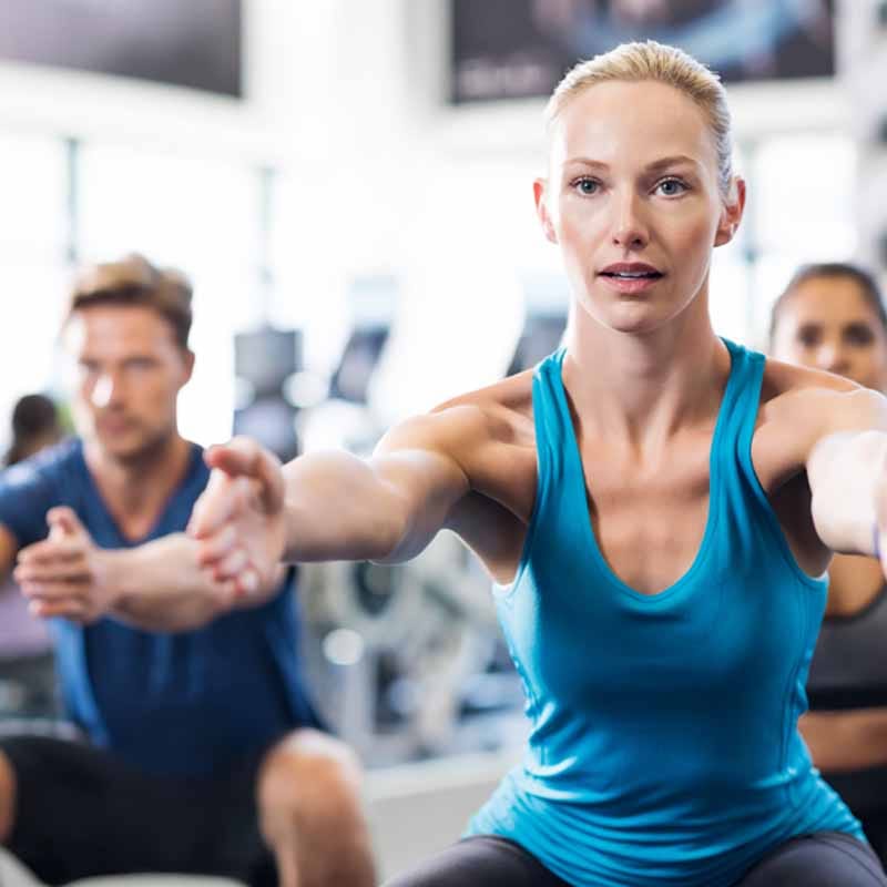 Vrouw in blauwe sporttop doet squat oefening tijdens groepstraining in moderne fitnessruimte