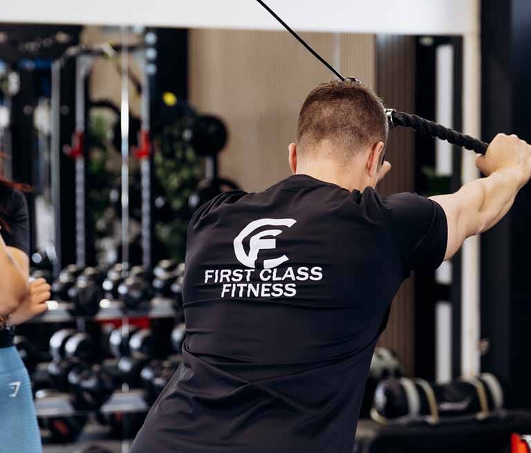 Man in trainingskleding voert treningsoefening uit met touw in fitnessruimte met halters en apparatuur