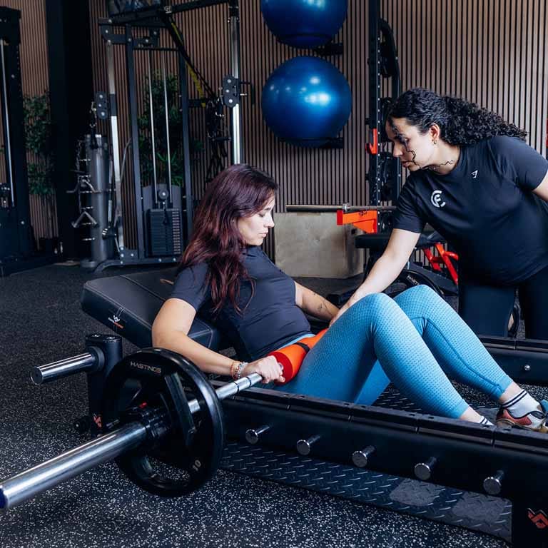 Personal trainer begeleidt vrouw bij haltertraining in moderne fitnessruimte