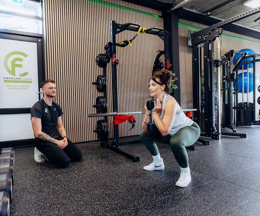 Personal trainer begeleidt vrouw bij squat oefening met halter in moderne fitnessruimte