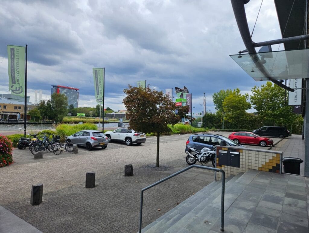 Parkeerplaats met auto's, fietsen en groen aan water met wolkenlucht