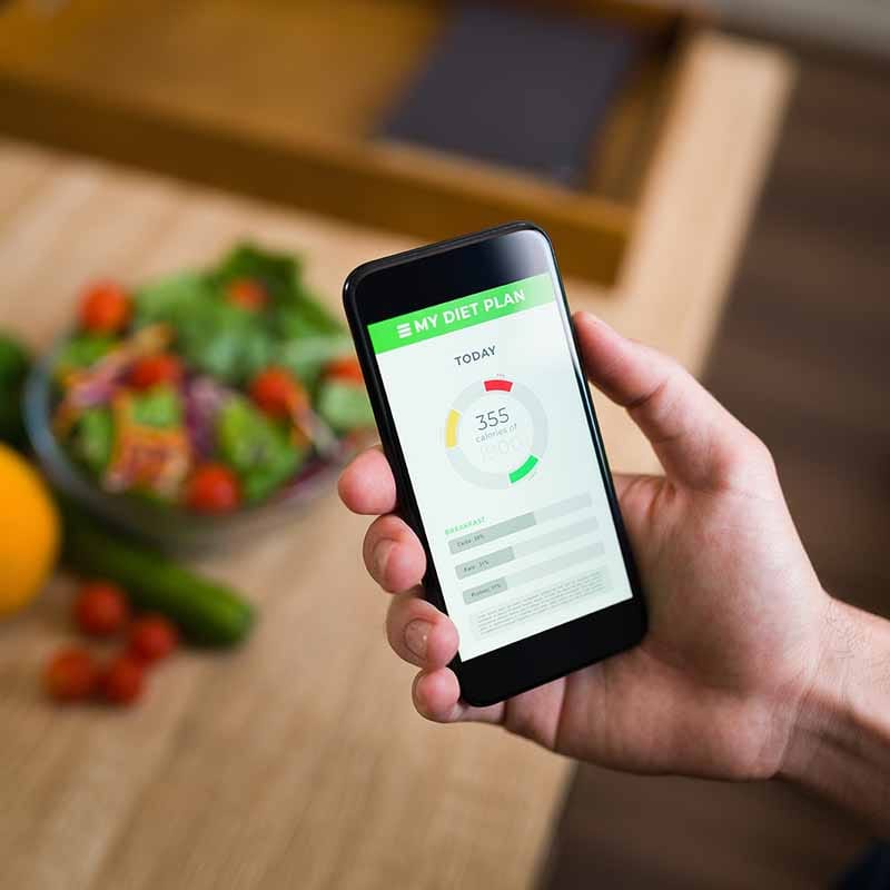 Hand houdt smartphone met MY DIET PLAN-app, 355 calorieën vandaag weergegeven, salade op houten tafel op achtergrond