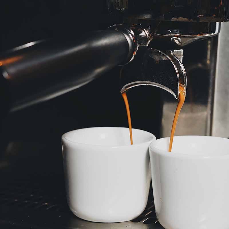 Espressomachine schenkt twee kopjes sterke koffie in witte kopjes