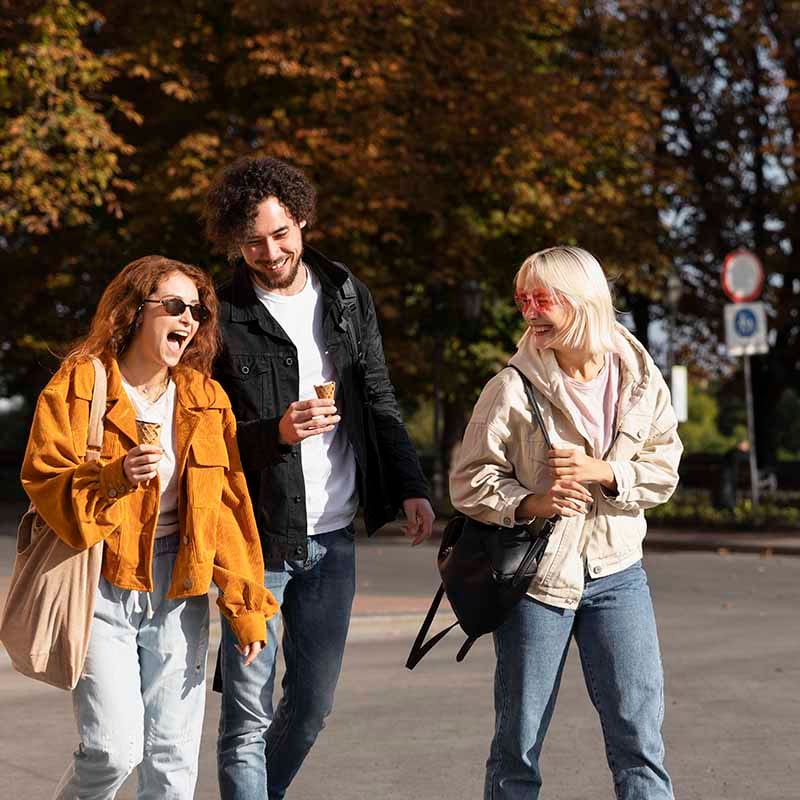 Drie mensen lopen lachend langs elkaar in een park met herfstkleuren