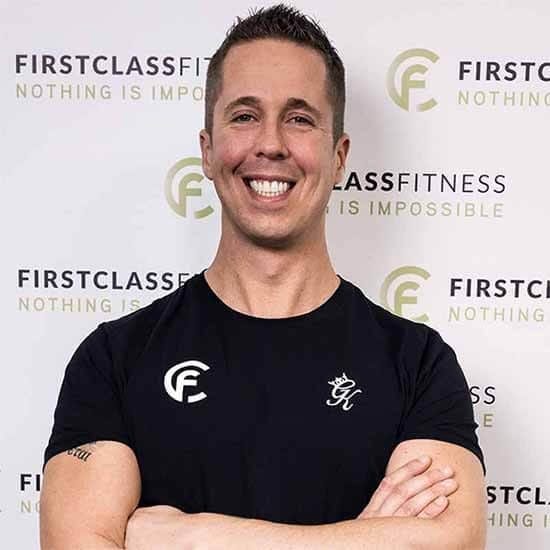 Personal trainer in zwart shirt met gekruiste armen glimlachend naar camera tegen First Class Fitness achtergrond