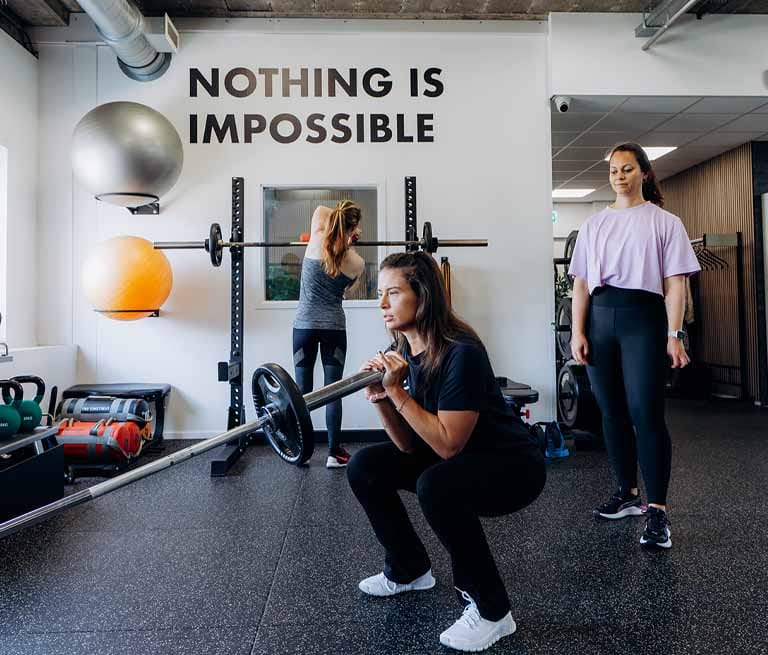 Drie vrouwen trainen in een fitnessruimte met de tekst 'Nothing is impossible' aan de muur
