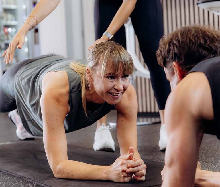 Vrouw in plank positie tijdens groepstraining onder begeleiding van instructeur