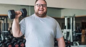 Man met bril in grijs shirt houdt halter omhoog in fitnessruimte