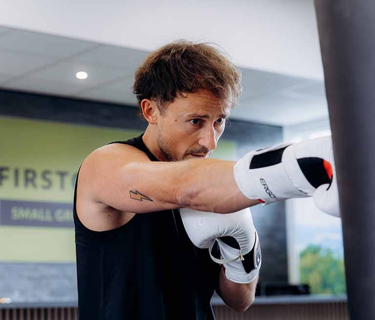 Man in zwarte sportkleding en witte bokshandschoenen oefent een directe slag in een trainingstudio
