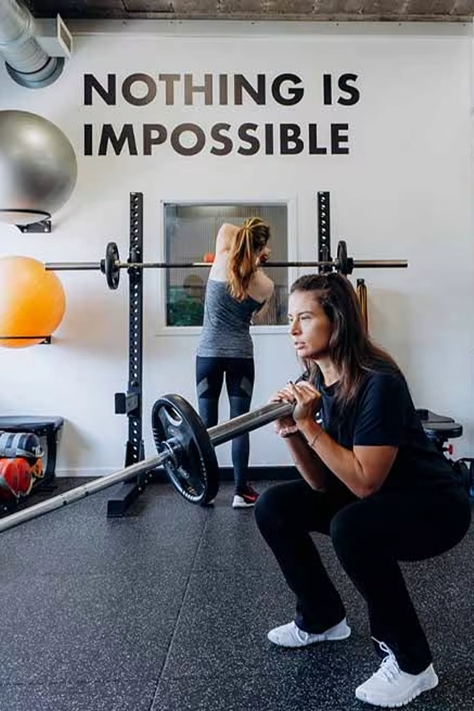 Twee vrouwen trainen met halters in een fitnessruimte onder de motiverende tekst Nothing is impossible