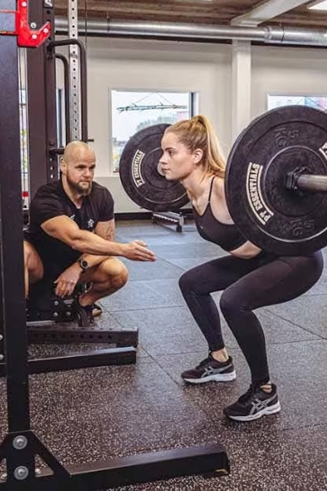 Personal trainer begeleidt vrouw met halter bij squatoefening in trainingstudio
