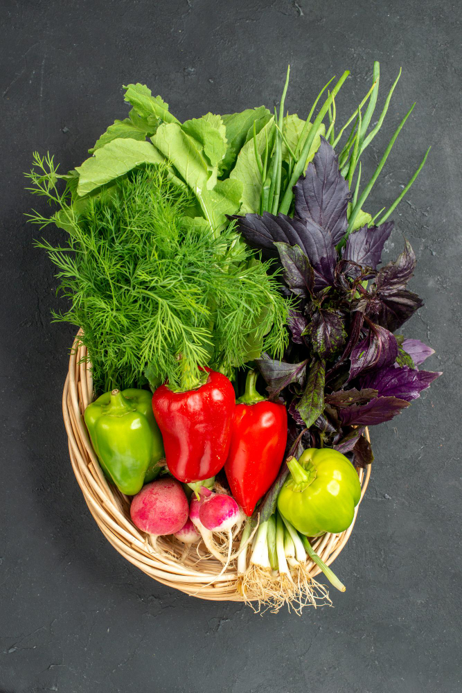 Mand met vers groente: sla, dille, groene en rode paprika's, radijsjes, groene appel en paarse basilicum op donkergrijze achtergrond