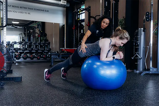 Personal trainer ondersteunt vrouw tijdens stabiliteitsbal oefening in fitnessstudio
