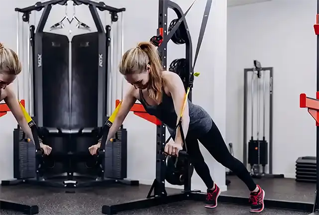 Vrouw in trainingskleding voert oefening uit aan fitnessmachine in moderne trainingstudio