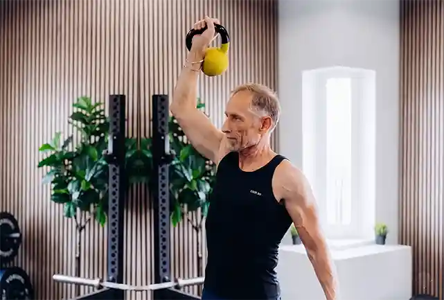 Man voert kettlebell-oefening uit in moderne trainingsstudio met groene planten
