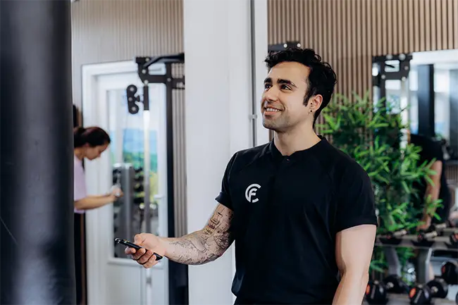 Personal trainer met tatoeages geeft instructies op apparatuur in moderne trainingsstudio