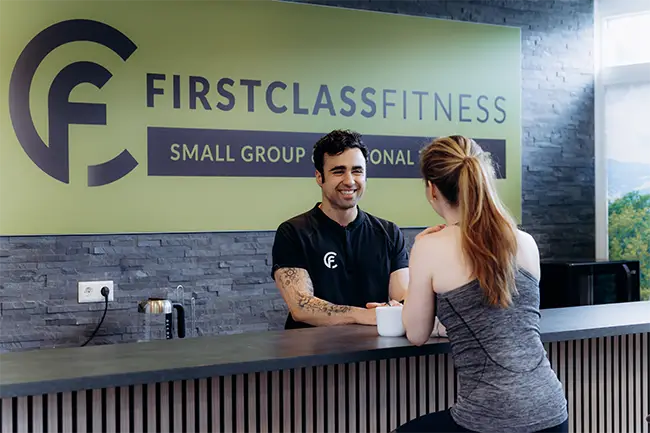 Trainer in zwart shirt begroet klant aan receptie van personal training studio