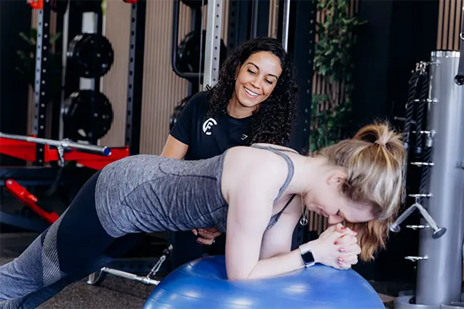 Personal trainer ondersteunt cliënt bij oefening op stabilisatiebal in fitnessruimte