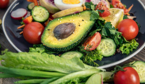 Gezonde maaltijd met halve avocado, tomaat, komkommer, sla en hardgekookt ei op donker bord