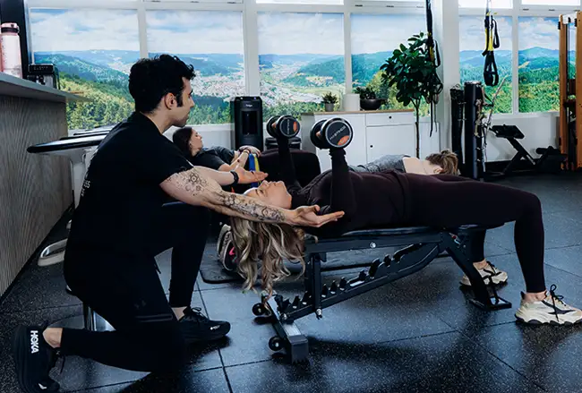 Personal trainer begeleidt vrouw bij oefening op trainingsbank in moderne studio met bergzicht