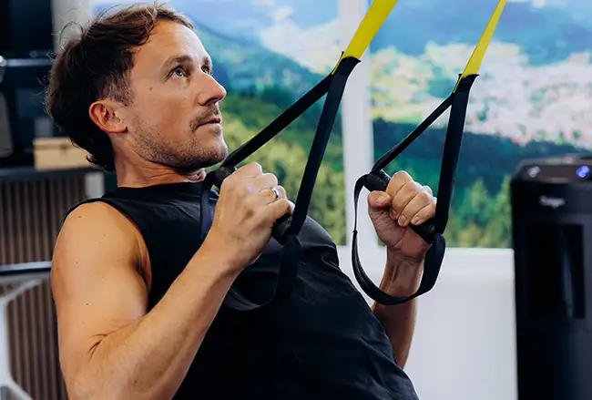 Man doet training met suspension straps tegen berglandschapachtergrond in fitnessruimte