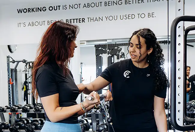 Twee trainers in zwarte shirts bespreken training in een studio onder het motto Working out is not about being better than you used to be