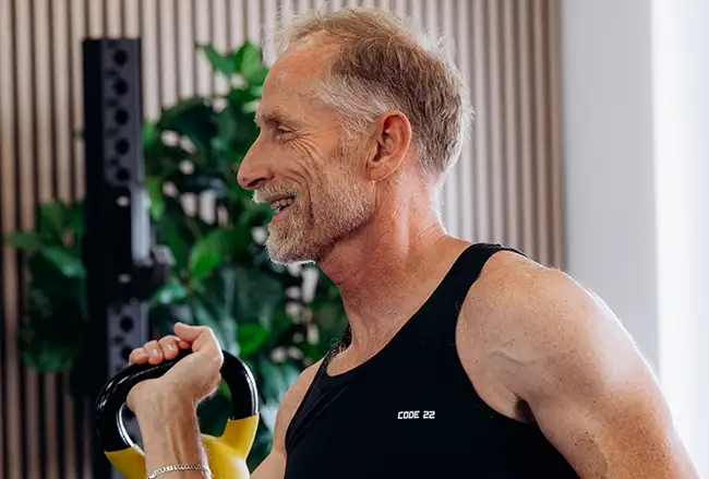 Man in CODE 22 tanktop met gele halters tijdens personal training sessie in moderne studio