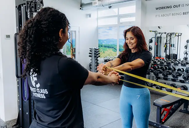 Twee trainers voeren samen een oefening uit met een gele elastische band in de fitnessruimte