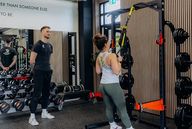 Personal trainer begeleidt vrouw bij training op multifunctioneel trainingsapparaat in fitnessruimte