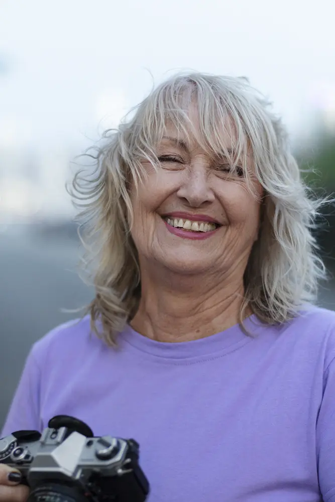 Vrouw in paars shirt lacht naar de camera terwijl ze een camera vasthoudt
