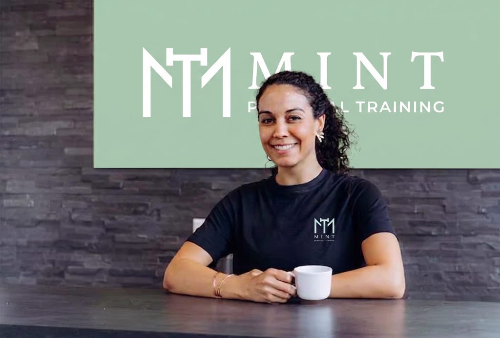 Vrouw in zwart Mint-shirt zit aan tafel met kopje koffie voor groene achtergrond met Mint Personal Training logo