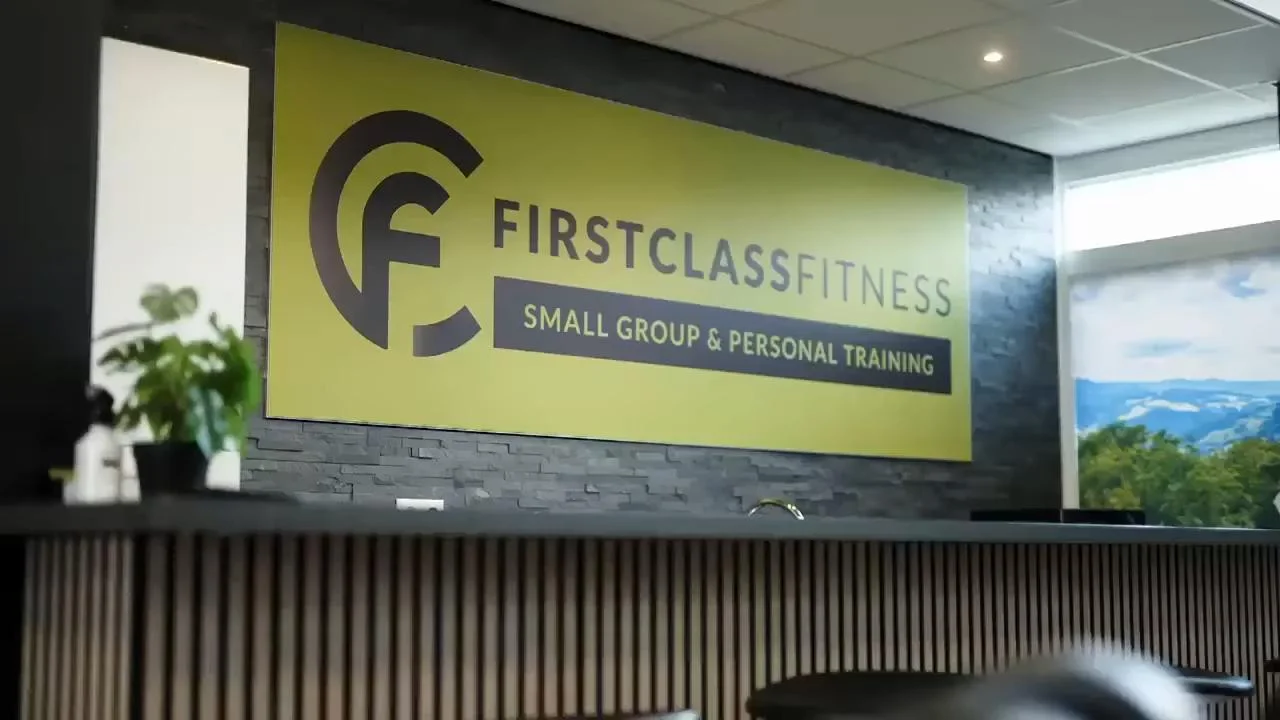 Gele binnensignage met donkergrijs logo en tekst 'SMALL GROUP & PERSONAL TRAINING' in moderne fitnessruimte